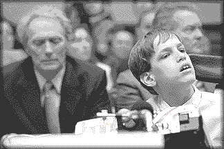 photo shows Kyle testifying via touch-talker, looking very intelligent and responsive, with Clint Eastwood seated behind him looking like he has a pain in his prostate