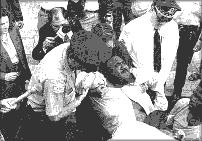 photo of an activist, apparently in some pain, being carried away by Chicago policemen.